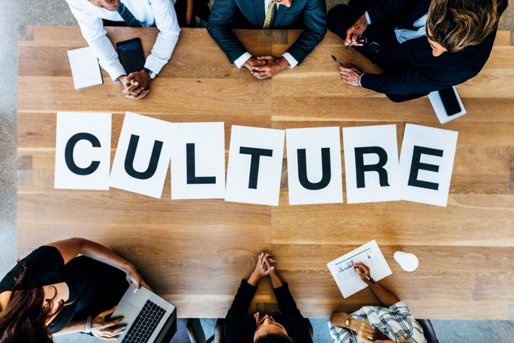 Group of business people with alphabets signs forming the word Culture on table. Top view of business people discussing over work culture in a meeting.