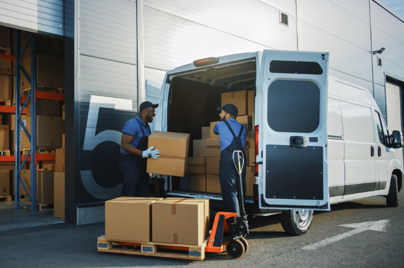 Outside of Logistics Distributions Warehouse: Two Workers Talk, Joke use Hand Pallet Truck Start Loading Delivery Truck with Cardboard Boxes, Online Orders, Purchases, E-Commerce Goods.